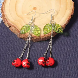 Detail of cherry skull earrings with red resin charms and green leaves on wood base