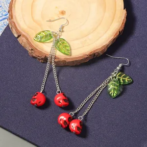 Macro detail of cherry skull long earrings with green leaves on a rustic wood slice