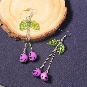 Detail of long cherry skull earrings with purple pendants and green resin leaves