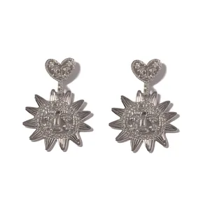Macro shot of silver sun flower earrings featuring heart charms and embossed face details