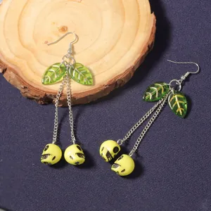 Macro detail of cherry skull earrings with green resin leaves and silver chain links