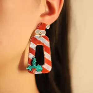 Boucles d'oreilles de Noël festives en acrylique avec chapeau rouge et houx portées par mannequin