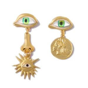 Macro shot of asymmetric gold long drop earrings featuring green eyes and coin portraits