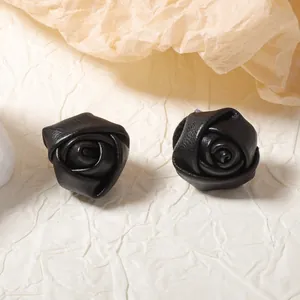 Elegant black leather rose stud earrings with petal texture on beige crinkled paper