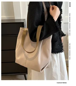 Detalle de un bolso tote grande de lona beige con asas verde oliva colgado al hombro