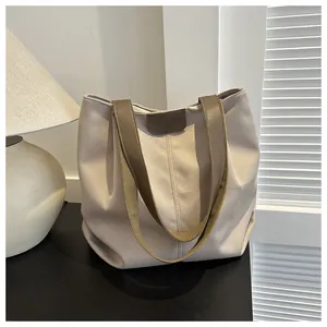 Detalle de bolso tote de lona con correas marrones sobre superficie negra y luz suave