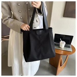 Detalle de bolso tote de lona negra con asas de cuero y solapa decorativa frontal