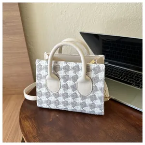 Detail of grey houndstooth plaid mini handbag with cream leather trim on a wooden table
