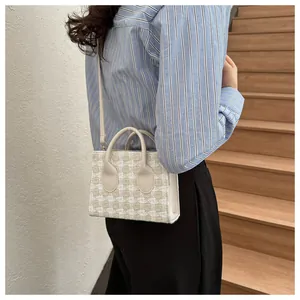 Close-up of a tweed plaid handbag featuring white leather handles and a woven texture