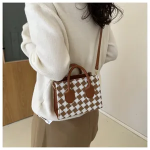 Close-up of brown plaid small square bag featuring leather handle and golden hardware