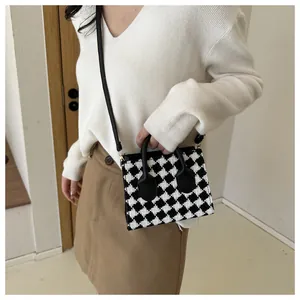 Close-up of small black and white houndstooth plaid crossbody bag with leather handle