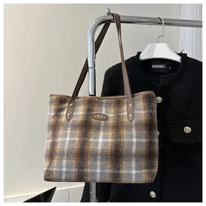 Detailed close-up of a plaid tote bag showing its woolen texture and metallic logo plate