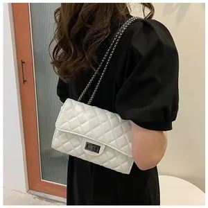 Detailed view of white quilted crossbody bag with metal chain strap and turn-lock closure