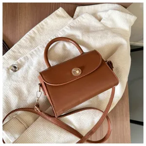 Detail of a brown leather crossbody bag featuring a gold rotary clasp and top handle