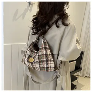 Dettaglio borsa hobo in tweed a quadri marroni con logo dorato su modella in trench