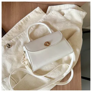 Detail of white structured crossbody bag with gold round clasp and top handle