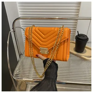 Close-up of orange quilted crossbody bag with gold chain strap and V-pattern faux leather