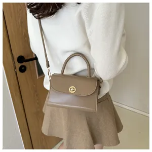 Detail of khaki leather mini crossbody bag featuring a round gold rotary clasp and top handle