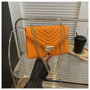 Detail of vibrant orange chevron quilted crossbody bag with gold chain strap and buckle