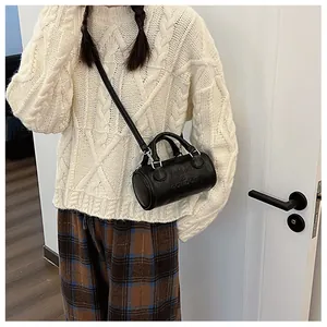 Detail of black cylinder bag with embossed letters worn with a white knit sweater