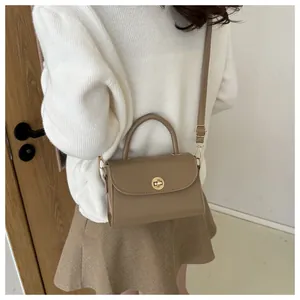 Close-up of taupe leather crossbody bag with a round gold metal twist lock and top handle