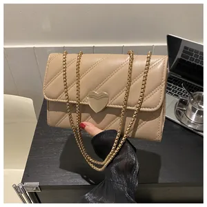 Detail of beige quilted crossbody bag with gold heart-shaped lock and metal chain