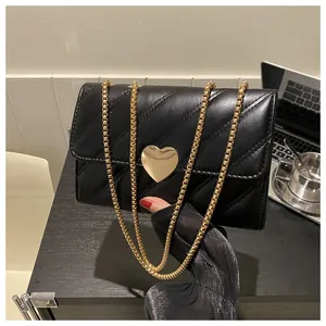 Close-up of black quilted small crossbody bag with a gold heart clasp and chain strap