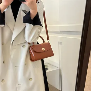 Minimalist brown leather small square bag with metal lock worn by a model in a beige coat