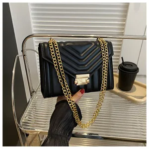 Detailed macro of black quilted V-pattern leather bag with golden metallic chain strap