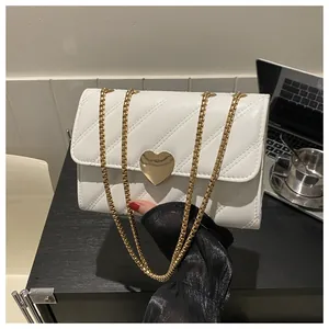 Detail of white quilted crossbody bag featuring a large gold heart-shaped metal twist lock