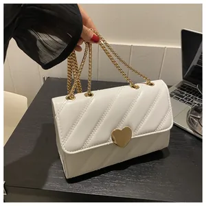Detail of white quilted crossbody bag featuring a golden heart buckle and chain strap