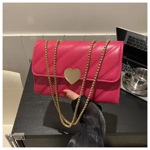 Close-up of fuchsia quilted crossbody bag with golden heart clasp and chain strap
