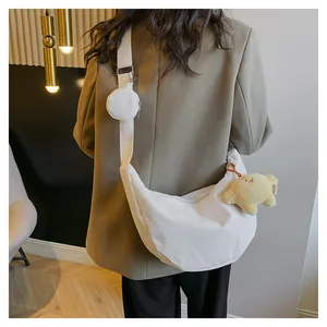 White corduroy crescent bag shown on model featuring a small round coin purse and bear charm