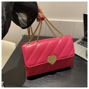 Detail of rose red quilted crossbody bag with gold heart clasp and metal chain strap