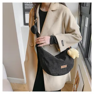 Close-up of black corduroy crescent bag with adjustable strap and bear plush charm