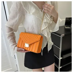 Close-up of bright orange quilted crossbody bag with golden chain and clasp detail
