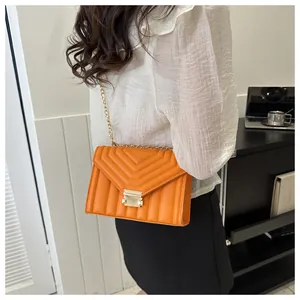 Detail of orange crossbody bag with V-shaped quilted pattern and gold chain strap