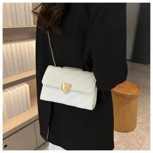 Detailed view of a white crossbody bag with heart clasp and gold chain strap on a model