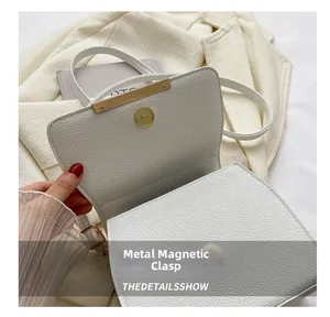 Detailaufnahme des goldenen Magnetverschlusses an einer weißen Handtasche aus Leder