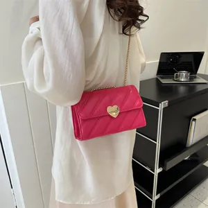 Hot pink quilted crossbody bag with gold heart clasp and chain strap shown on model