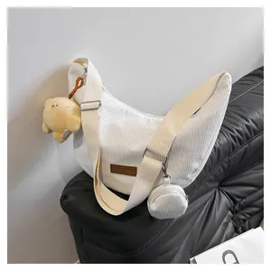 White corduroy crescent bag detail with mini pouch and plush bear charm on leather sofa