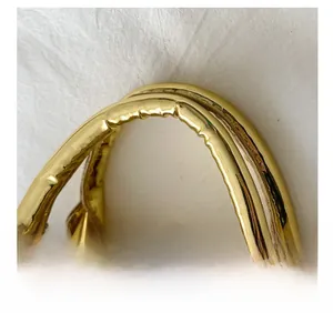 Detail of glossy gold shell bag featuring a sturdy handle and secure double metal zippers