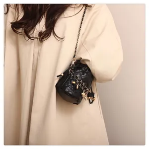 Détail d'un mini sac seau noir matelassé avec chaîne dorée et pendentif en cœur chic