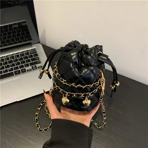 Petit sac seau matelassé noir avec chaîne dorée et pendentifs cœurs en main