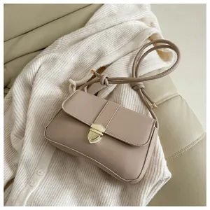 Detail einer beige Kunstleder-Mini-Tasche mit Goldverschluss auf weichem Strickhintergrund
