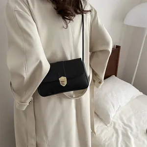 Schwarze Leder-Umhängetasche mit goldener Schnalle zu einem beigen Trenchcoat