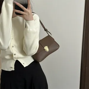 Braune Leder-Umhängetasche mit goldener Schnalle, von Model an der Schulter getragen