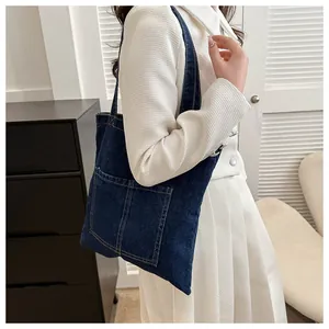 Détail du sac cabas en denim bleu foncé avec deux poches avant porté par un mannequin