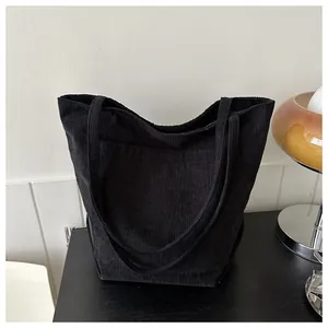 Nahaufnahme der schwarzen Cord-Tote-Bag auf dunklem Holztisch mit Retro-Lampe