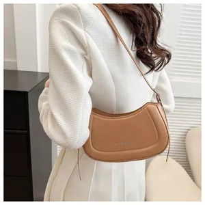 Détail du sac demi-lune en cuir beige avec texte embossé sur un blazer blanc